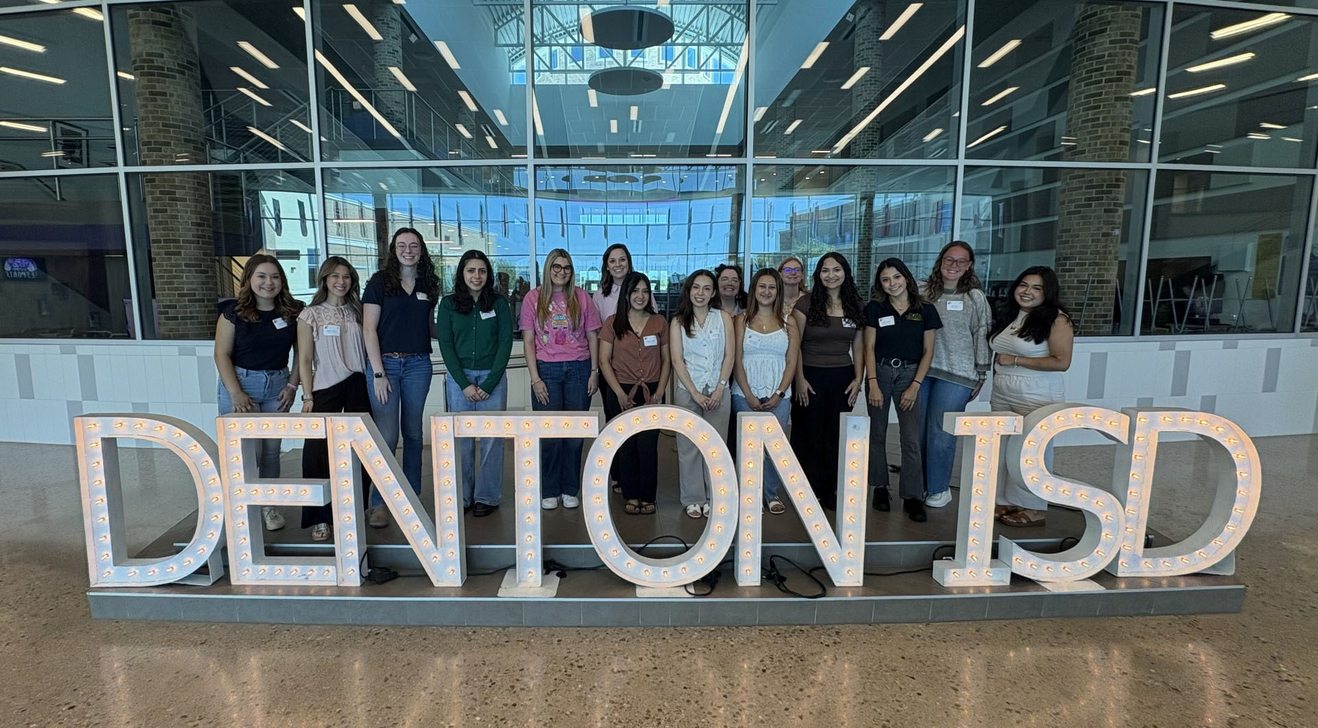 Group of students with large Denton ISD logo in front of them