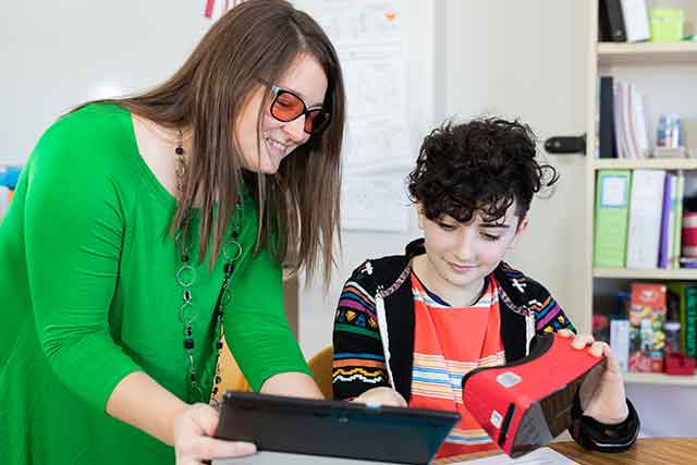 Dr. Lauren Eutsler demonstrates the use of virtual reality goggles to a 6th grade student. 