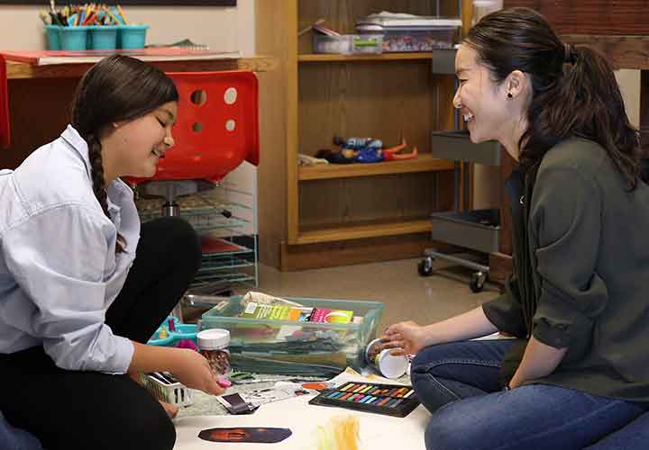 A girl draws with chalk while talking with a UNT counselor. 