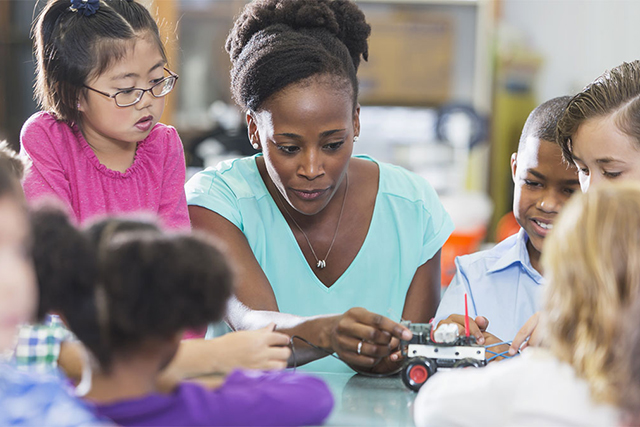 A teacher demonstrates a remote controlled vehicle to children in a classroom 