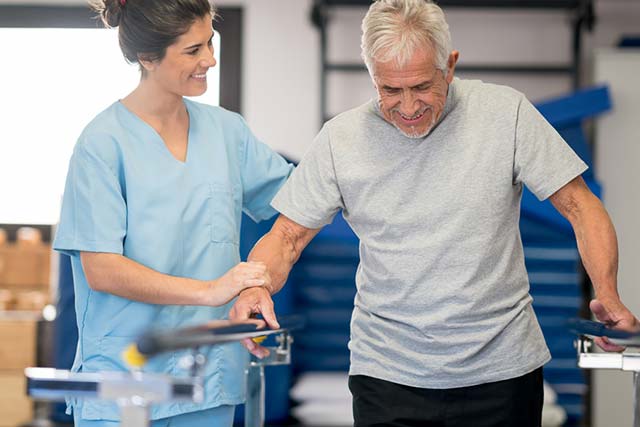 Physiotherapist and senior patient working on the parallel bars at a physical rehabilitation clinic.