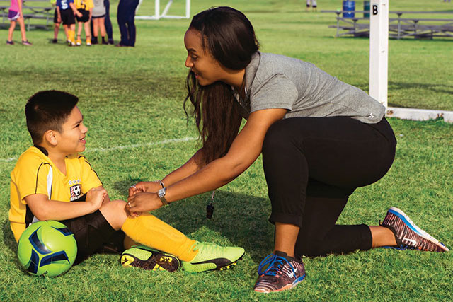 A woman ties a show for a young soccer player.