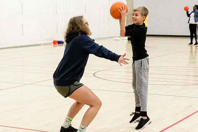 A young boy attempts to shoot a basketball over the head of a UNT student during a class on campus.