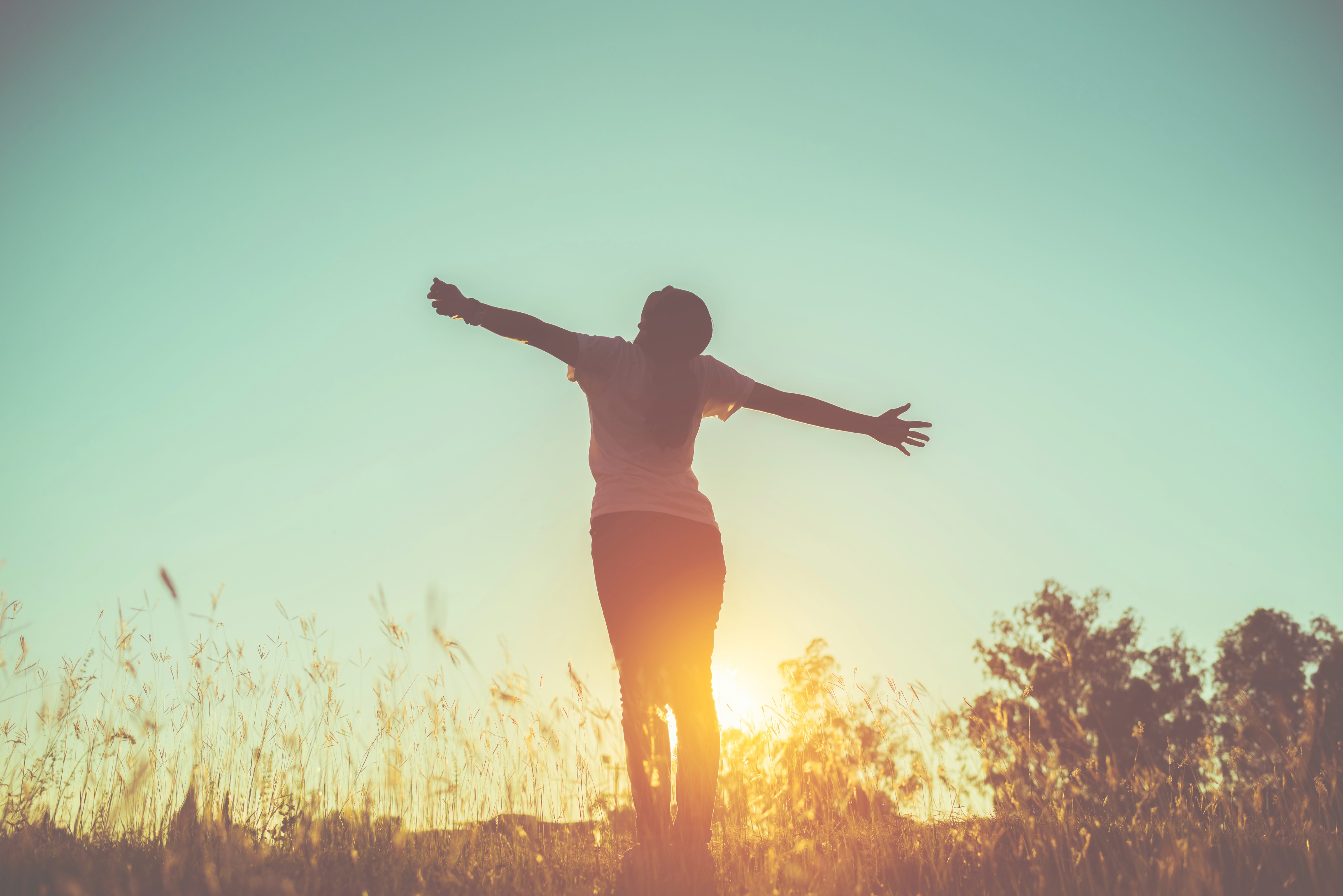 Person standing outside with arms outstretched as the sun is rising.