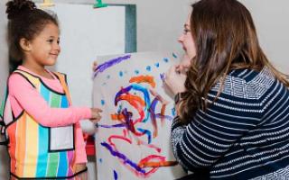 A child paints on paper while a therapist looks on