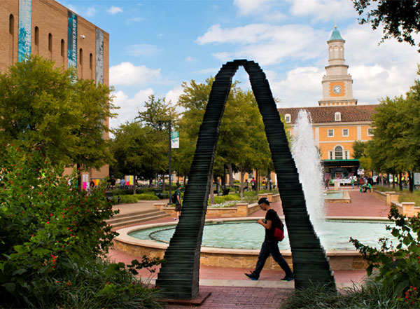 A UNT student walks between the arch and fountain outside Willis Library